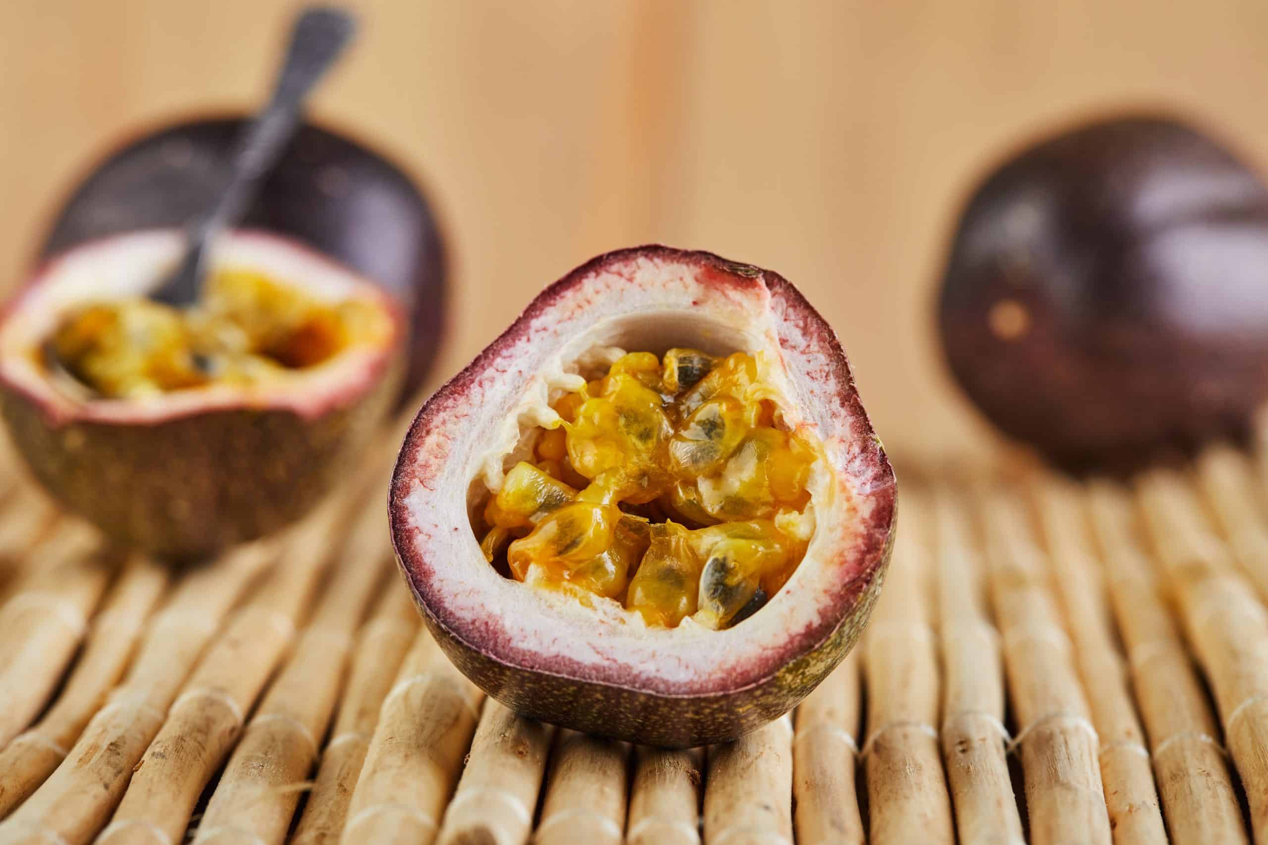 Passiflora is cut into two halves with a spoon inside and two whole on a bamboo background. Side view.